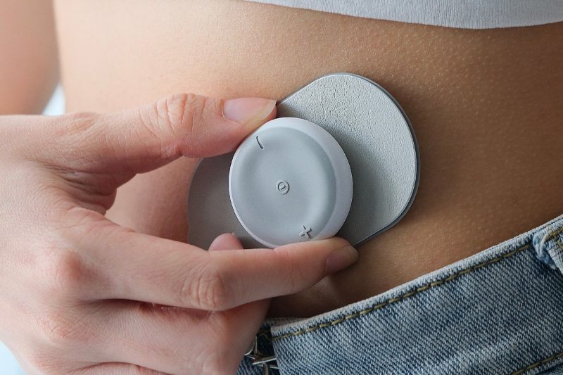 Woman applying the Pod Pro Controller on her lower abdomen area for period cramps relief.

